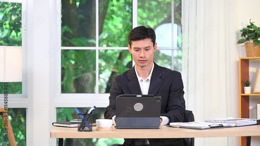 Confident businessman in suit walking to window after finishing working on his digital tablet Confident businessman in suit walking to window after finishing working on his digital tablet