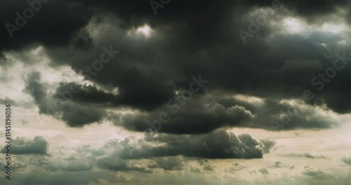 Timelapse of menacing dark grey clouds flying in the overcast sky and letting through some rays of sunlight creating strange underwater feeling to the scenery