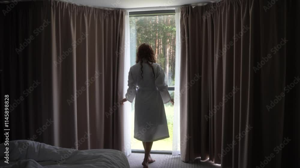 Slow motion of woman in robe opens curtains in room, revealing forest view outside. Wake up at the morning, weekend vacation on nature. Designed luxury home interior. self-care, new day starting