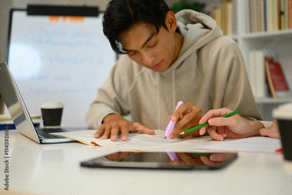 Focused male student highlighting important text with a marker while studying with his tutor Focused male student highlighting important text with a marker while studying with his tutor