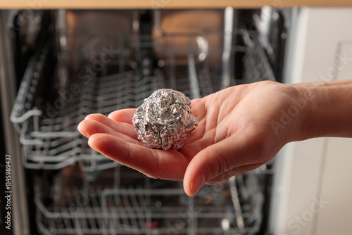 Obraz na płótnie A woman puts a ball of aluminum foil into the dishwasher, cost-effective, enviro