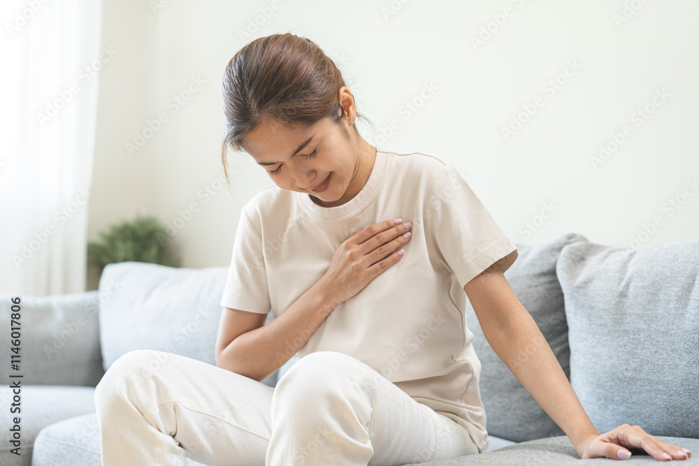 Heart attack, health care concept, suffering acute cardiac asian young woman hand touching on her chest pain, breathing problem, asthma attack, pressure while sitting on sofa with closed eyes at home. Heart attack, health care concept, suffering acute cardiac asian young woman hand touching on her chest pain, breathing problem, asthma attack, pressure while sitting on sofa with closed eyes at home.