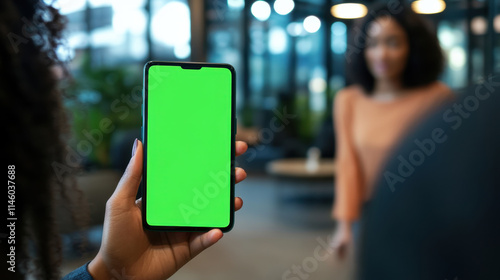 Woman holding smartphone with green screen in modern office building lobby