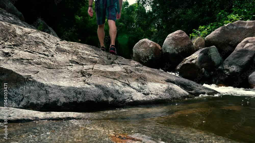 A tourist crosses a stream and climbs over rocks in the jungle A tourist crosses a stream and climbs over rocks in the jungle