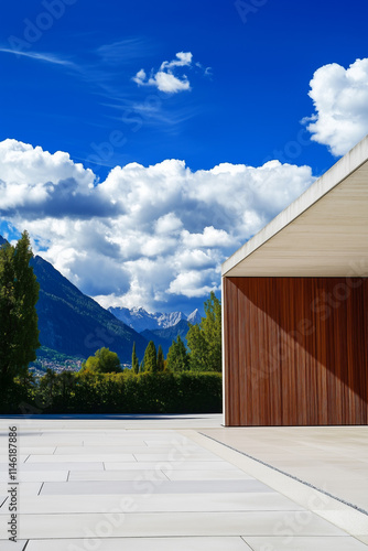 Spacious terrace in front of a modern building with wooden and concrete elements. The terrace and the house are located in an alpine setting