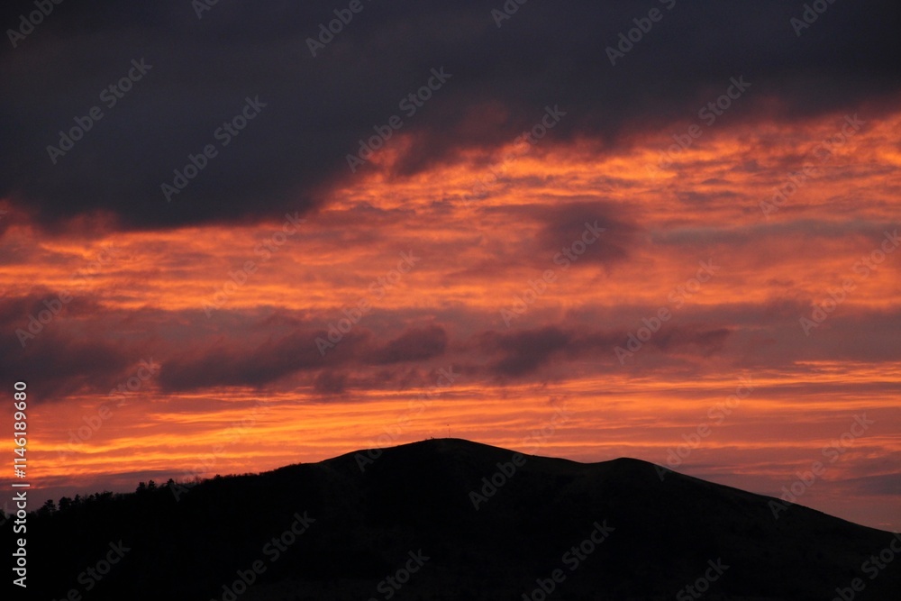 Obraz premium colorful sky at sunrise with a small hill in the foreground