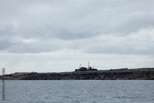 Rusting shipwreck on a rocky island coast, overcast sky.  Coastal scene with water and gray clouds. photo