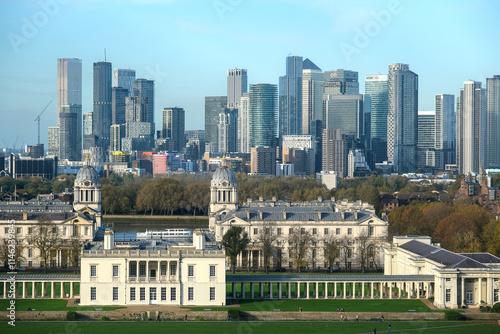 The Old Royal Naval College, framed by trees and green lawns, contrasted against the towering glass skyscrapers of Canary Wharf under a clear sky. London. photo