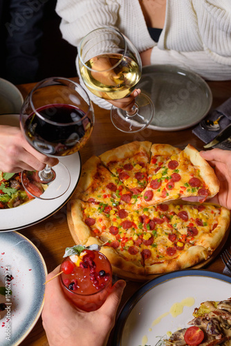 a group of friends holds wine and cocktail in their hands against the background of a table with food