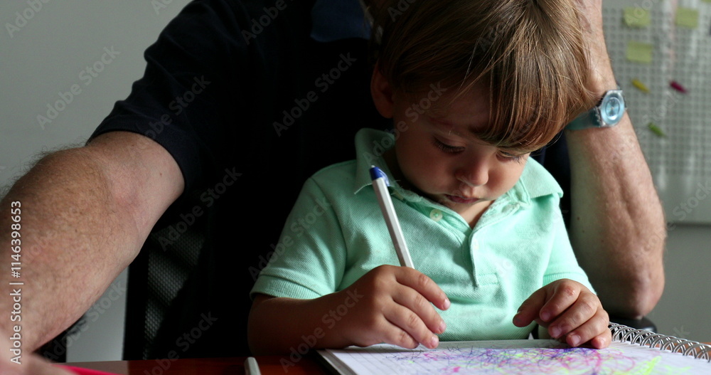 Naklejka premium Little toddler boy doodling on paper while sitting on grand-father lap