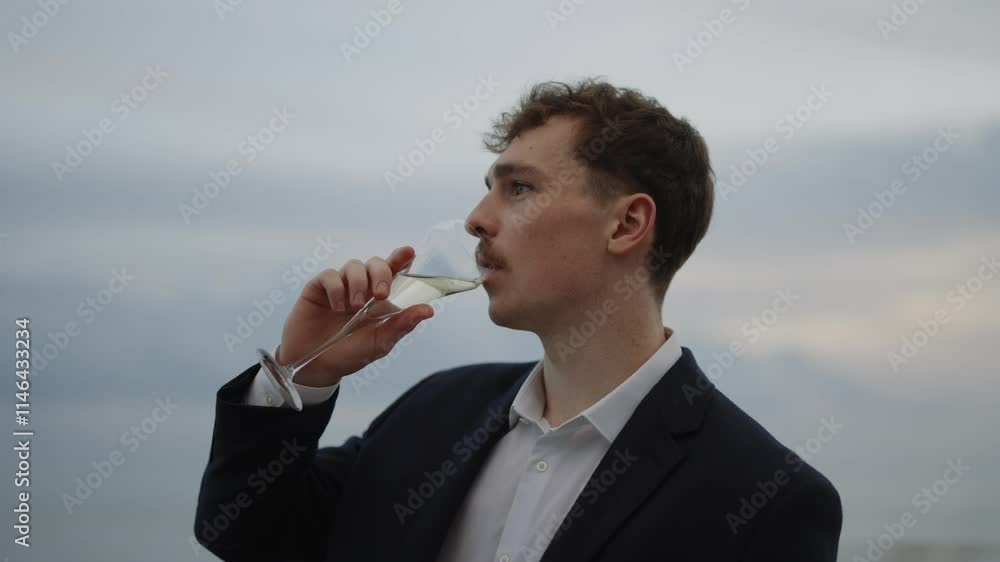 A man in a suit is drinking from a wine glass. Concept of sophistication and elegance, as the man is dressed in a suit and holding a glass of wine. The setting appears to be a formal or upscale event A man in a suit is drinking from a wine glass. Concept of sophistication and elegance, as the man is dressed in a suit and holding a glass of wine. The setting appears to be a formal or upscale event