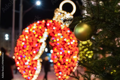 Glow of festive light decorations on the street in the city. Glowing colored garlands and ball on the New Year tree. Soft selective focus photo