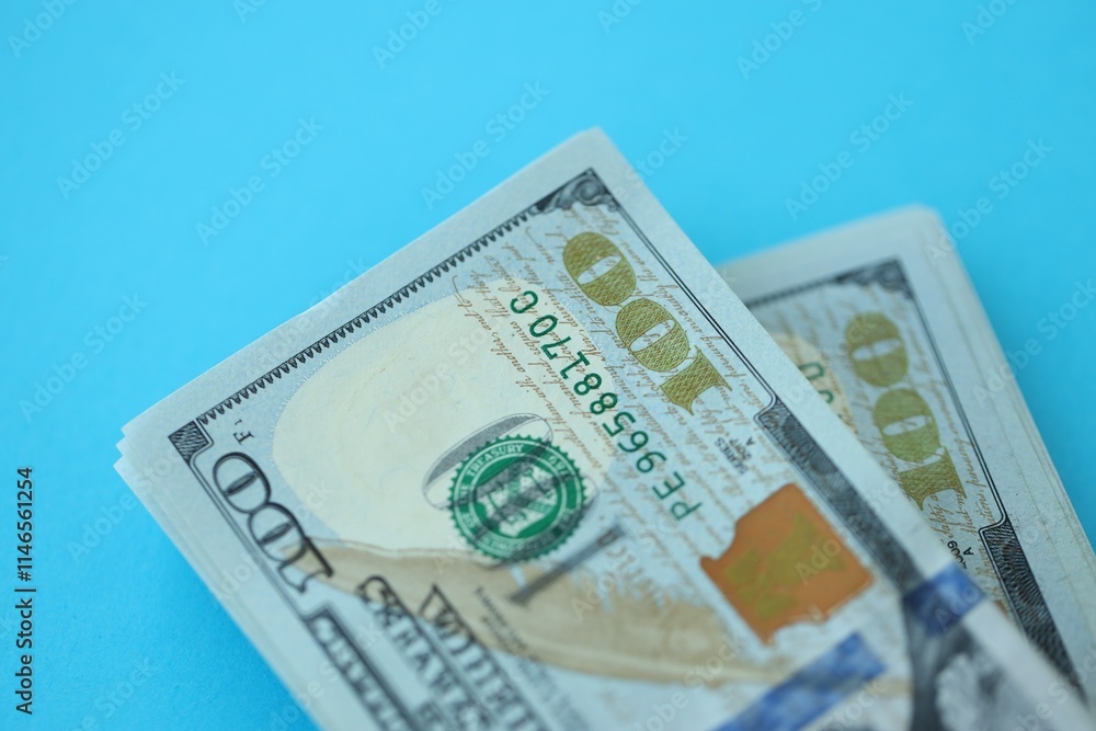 Big amount of hundred dollar bills in thick stack lies on bright blue color paper background Big amount of hundred dollar bills in thick stack lies on bright blue color paper background
