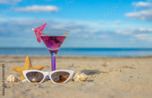 Canvas Print Glass of cocktail on sandy beach and sunglasses next to sea