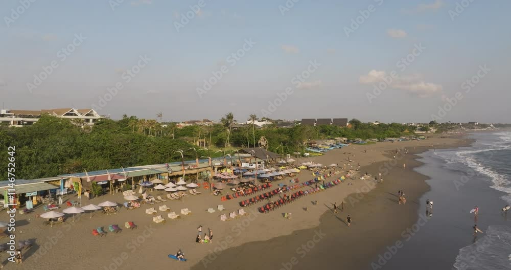 Tourists relax on sandy beaches under umbrellas watching sunset, aerial of Canggu beach, serene coastal waves, and tropical waterfront scenery Tourists relax on sandy beaches under umbrellas watching sunset, aerial of Canggu beach, serene coastal waves, and tropical waterfront scenery