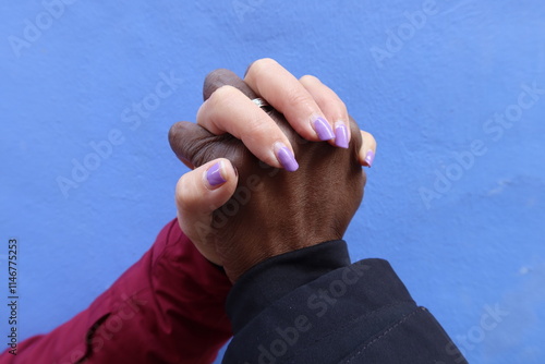 Alcoy, Alicante, Spain, December 19, 2024: Intertwined hands of a couple of a white girl and a black boy on a blue wall..Hands of a multiethnic couple photo