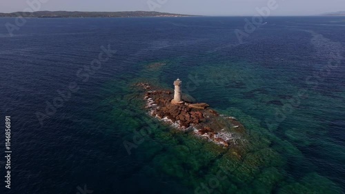 Faro Mangiabarche’s white tower shines against calm Sardinian seas. The drone captures rugged rocks, soft waves, and bright sunlight painting a tranquil coastal portrait. photo