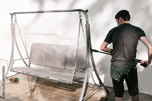 A young guy washes a garden swing with a kercher.