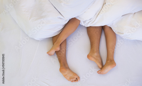 couple lies intertwined under soft white bedding, their legs playfully tangled. The scene conveys intimacy, relaxation, and warmth, suggesting a moment of comfort and connection, copy space photo