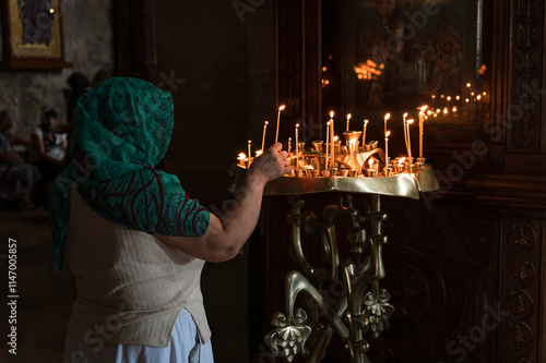 a woman lights a candle in front of a holy image in an Orthodox church in Svetitskhoveli Cathedral in Mtskheta, Georgia