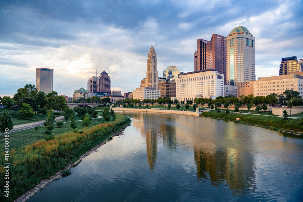 Scenic view of downtown Columbus, Ohio, during a calm evening with soft lighting, the skyline with modern skyscrapers and historic buildings reflecting in the Scioto River in the foreground Scenic view of downtown Columbus, Ohio, during a calm evening with soft lighting, the skyline with modern skyscrapers and historic buildings reflecting in the Scioto River in the foreground