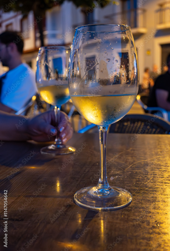 Obraz premium Two glasses of cold dry white wine served outdoor in cafe at night in historical Triana district, Sevilla, Spain, close up