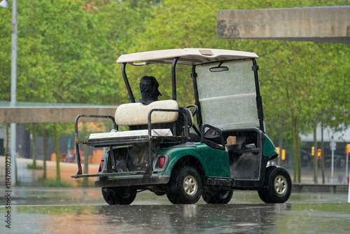 Empty golf cart with an umbrella on a rainy day. The cart is parked on a wet path with green trees in the background. Perfect for travel, leisure, and golf-related themes