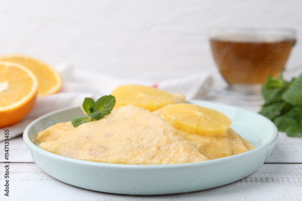 Delicious Crepes Suzette, mint, tea and oranges on white wooden table, closeup Delicious Crepes Suzette, mint, tea and oranges on white wooden table, closeup