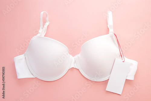 White women's bra with white paper label on pink background
