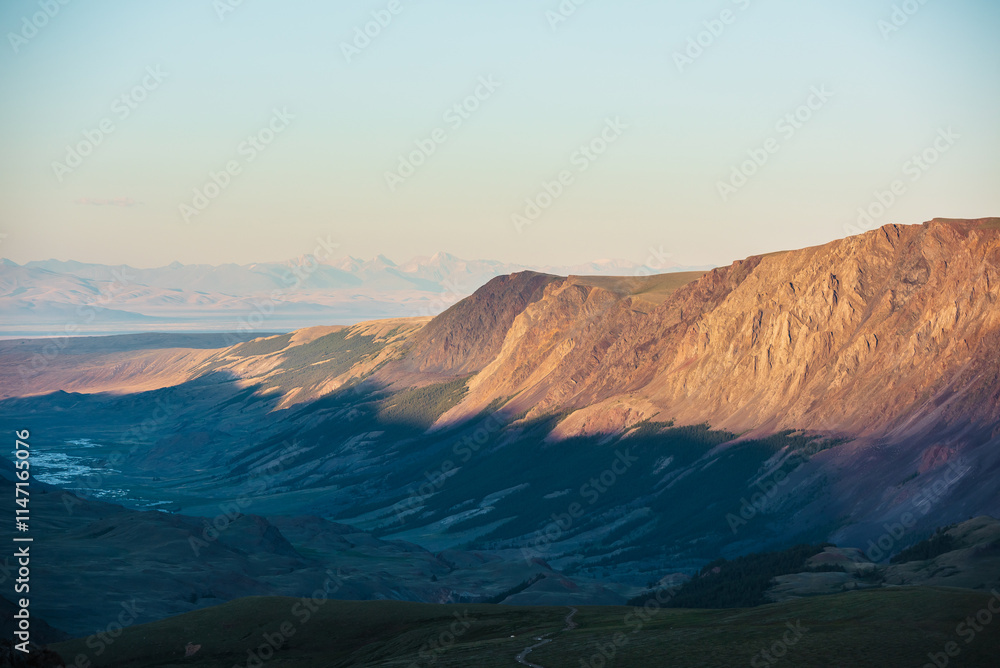 Fototapeta premium Scenic aerial top view to gold sheer crags on mountain ridge, illuminated by setting sun under clear sky in golden sunset tones. Evening alpine landscape in sunset color. Light and shadow in mountains