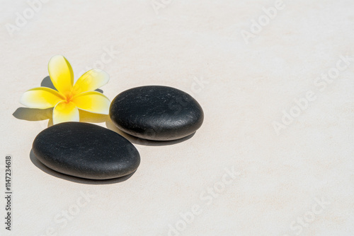 Two black stones on a white background with a yellow flower in the foreground photo