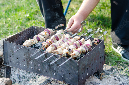 A close-up image of pork and onion skewers grilling over charcoal on a metal grill. With hand turning them over. photo