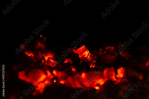 A close-up shot of glowing red hot coals in a fireplace. The fire has died down, leaving behind embers that still give off a warm glow.