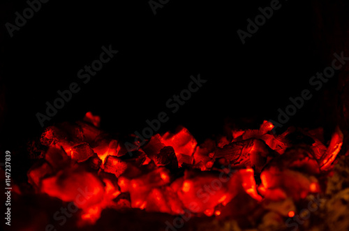 A close-up shot of glowing red hot coals in a fireplace. The fire has died down, leaving behind embers that still give off a warm glow.