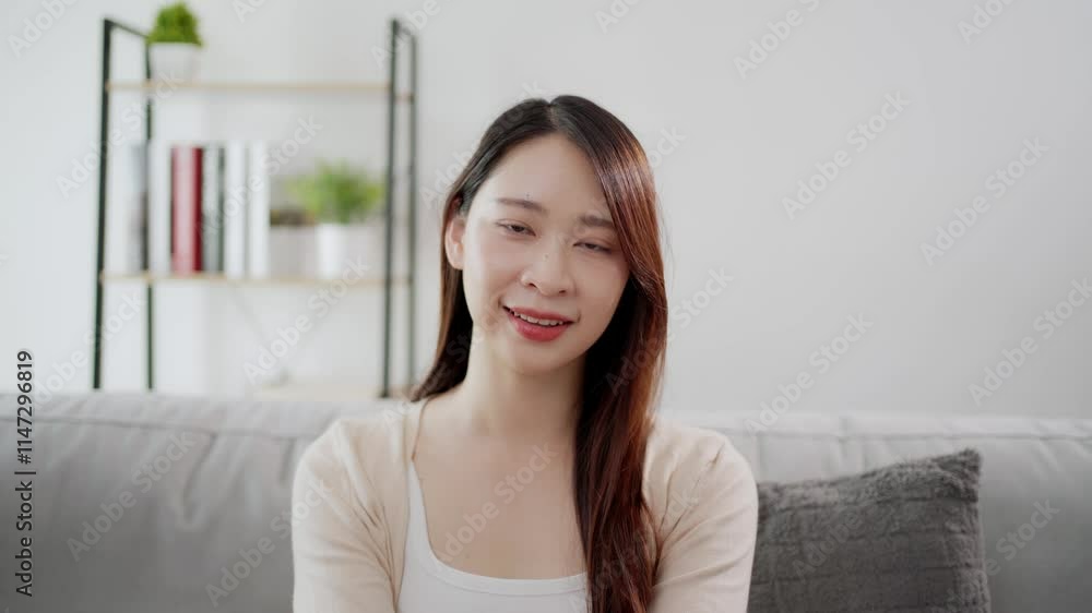 Video portrait of a beautiful and lovely Asian woman, looking at the camera with confidence, in a happy, cheerful mood, sitting on a sofa in a living room. Video portrait of a beautiful and lovely Asian woman, looking at the camera with confidence, in a happy, cheerful mood, sitting on a sofa in a living room.