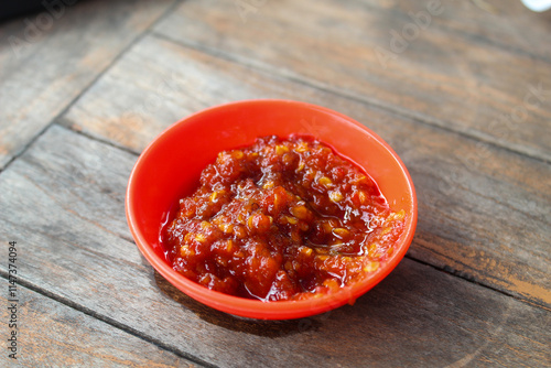 Portrait of sambal ulek or sambal terasi in small orange bowl on wooden table background. photo