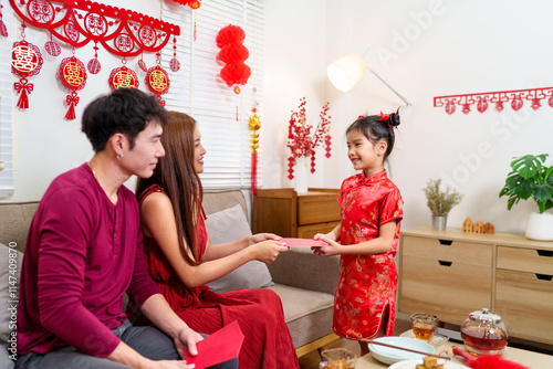 A child joyfully receives a red envelope (angpao) from parents during a Chinese New Year celebration, symbolizing blessings and good fortune photo