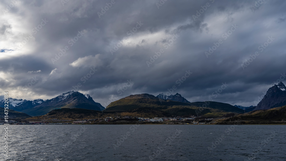 Beautiful mountain range. View from the ocean. Snow-capped peaks against a cloudy sky. The city of Ushuaia is located on the shore,at the foot of the hills.Ripples on the blue surface of the Channel  