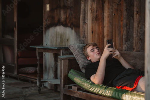 Teenage boy relaxing on outdoor lounge using mobile phone photo