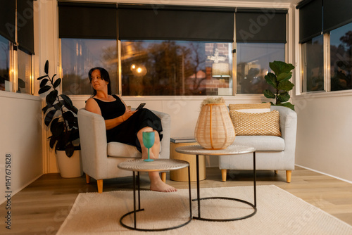 Woman in black dress looking out window from cosy armchair in warmly lit room