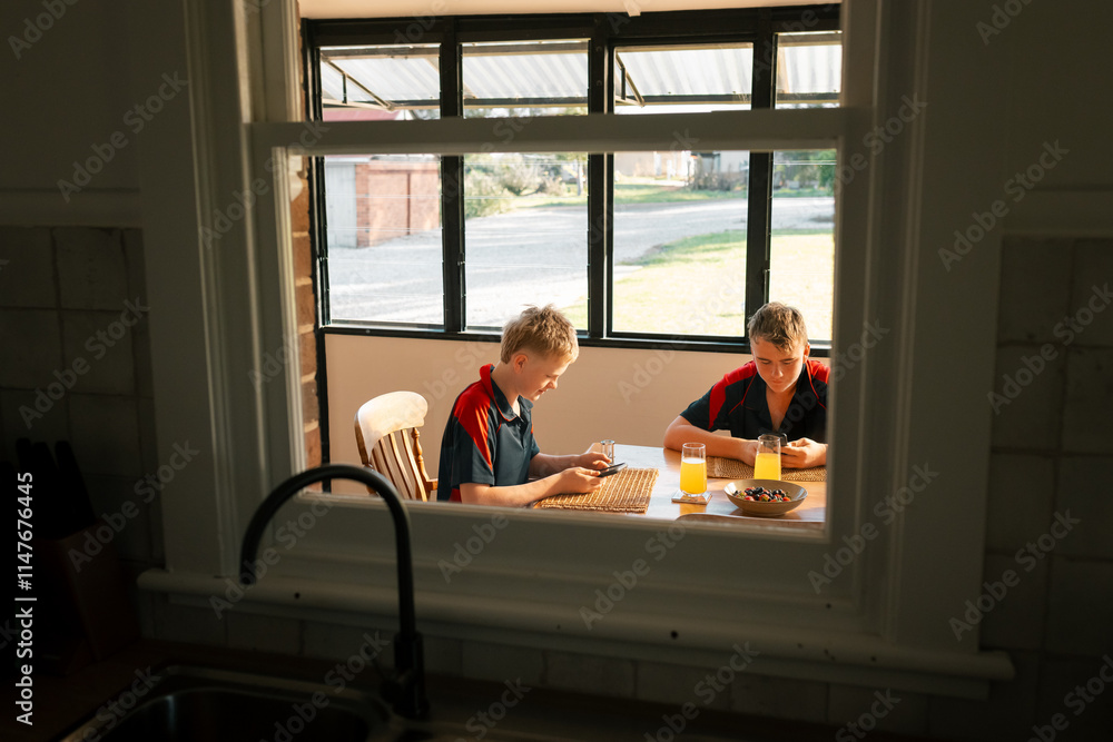 Boys in school uniforms at dining table focused on phones at breakfast time Boys in school uniforms at dining table focused on phones at breakfast time