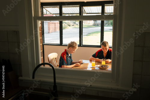 Boys in school uniforms at dining table focused on phones at breakfast time photo