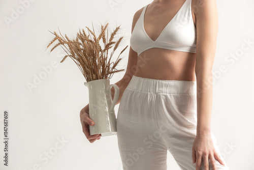 Young woman holding ceramic pitcher with wheat spikes bouquet, Celiac Disease And Gluten Intolerance	 photo