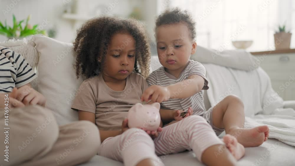 African American kids playing with ceramic piggy bank, family budget, save money . Happy little diverse children putting coins into money box, sitting together on soft couch in living room, childhood African American kids playing with ceramic piggy bank, family budget, save money . Happy little diverse children putting coins into money box, sitting together on soft couch in living room, childhood