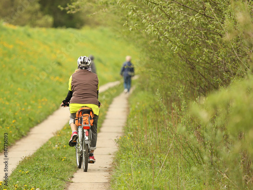 An old gray-haired woman rides a bicycle among the greens. A healthy and active part of life. Ecological transport for the population. Free time for retirement. Movement in space. Sports for the elder
