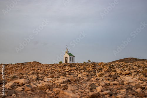 Small white wooden chapel in a monotonous rocky volcanic landscape. Church at sunrise. Twilight, sky coloring. Ermita Protestante de Violante, Fuerteventura, Canary Islands, Spain photo