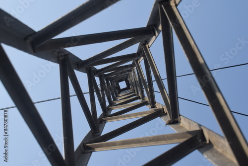 Steel structure of a high voltage pylon with wires, insulators blue sky and sun seen from underneath in frog perspective with vanishing point bottom view of an electrical tower structure