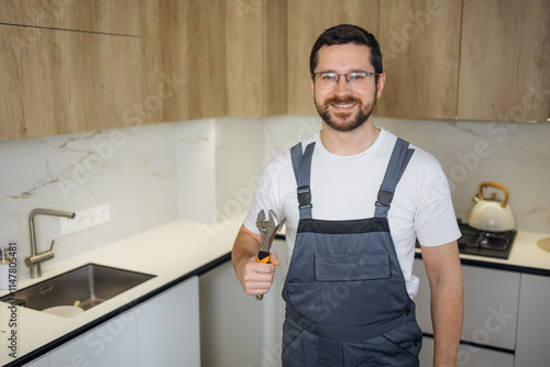 Young plumber holding pipe wrench in kitchen photo