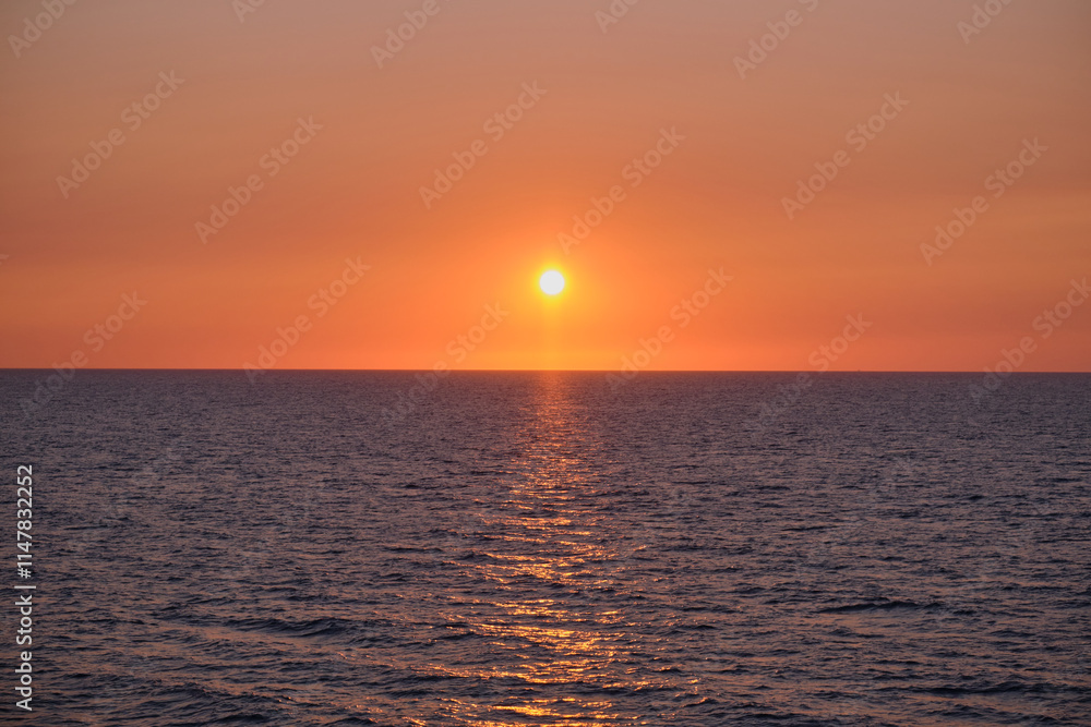 Fototapeta premium Panorama of sea sunrise, ocean sunrise, seascape. Romantic colorful sunset at the sea. The sun touches horizon. Bright sunset with large yellow sun under the sea surface.