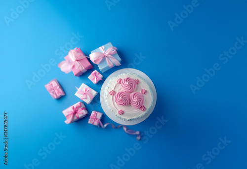 A single-tiered cake with pink frosting and a heart design sits atop a blue background surrounded by small wrapped gifts. photo